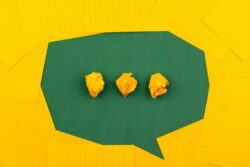 A green speech‑bubble shape on a yellow background contains three crumpled paper balls.