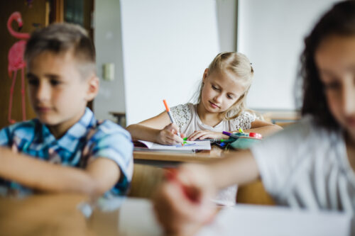 Child writing in a notebook during a classroom lesson.