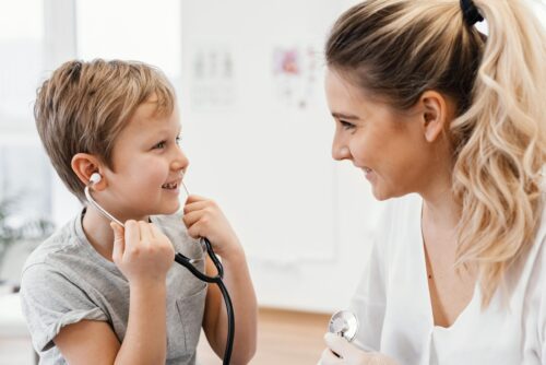 A child holds a stethoscope to their ear while an adult nearby holds another stethoscope during a play activity.