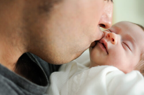 An adult gently kisses a baby’s face while holding the baby close.