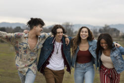 Four people walk outdoors with their arms around each other.