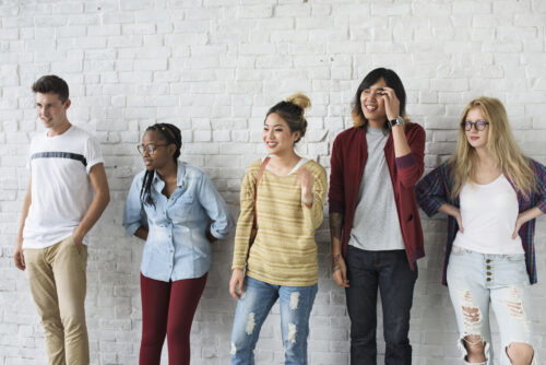 Five people stand in a row against a white brick wall.