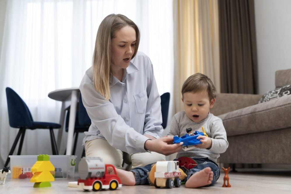 An adult sits on the floor helping a child play with toy animals and vehicles in a living room.