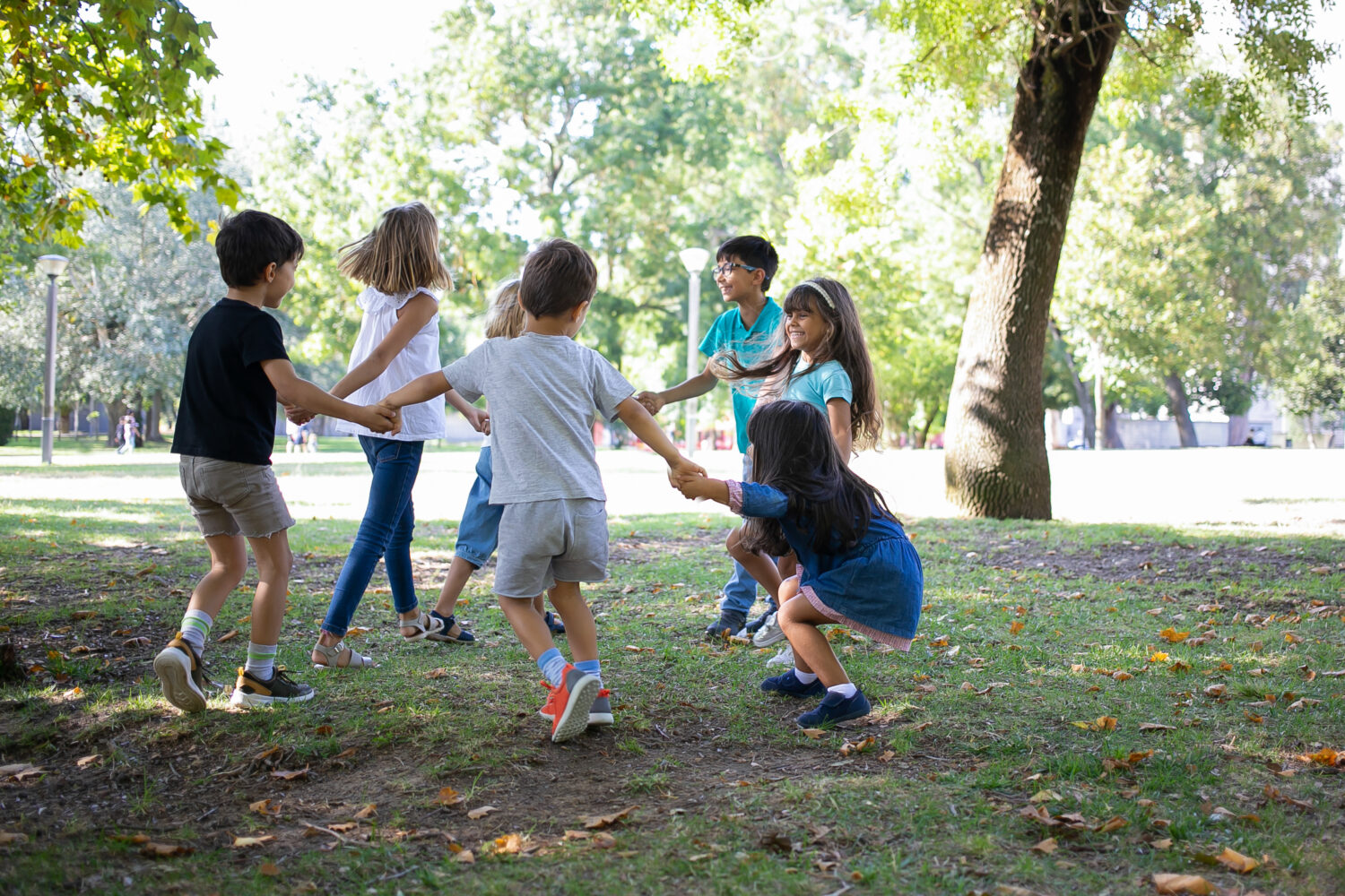 Children hold hands and play in a circle outdoors in a park.