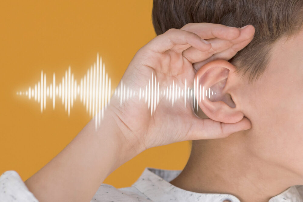 A close-up of a hand cupped behind an ear with a soundwave graphic on a yellow background.