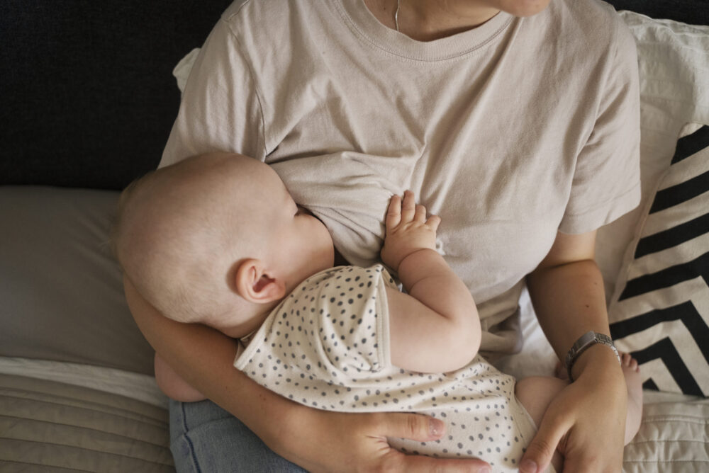 A baby is breastfed while being held on an adult’s lap indoors.