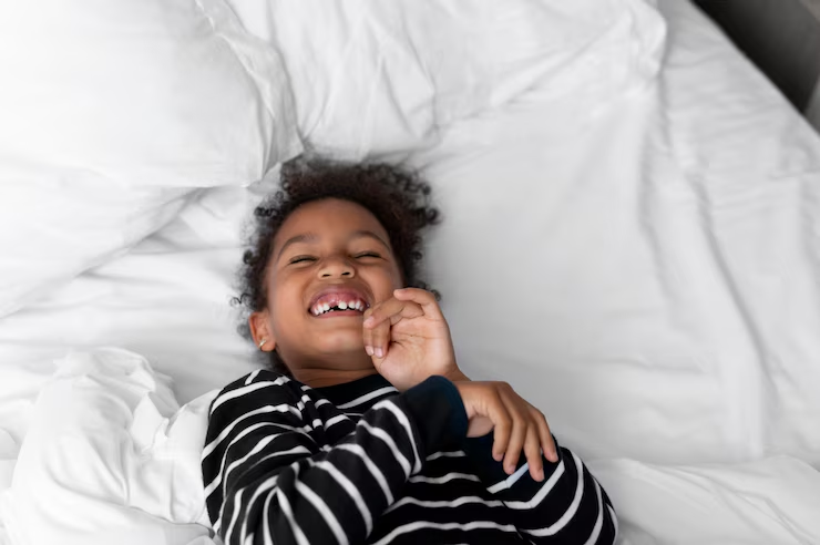 A child lies on a bed with white bedding, one hand raised near the face.