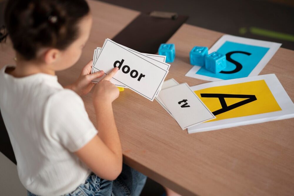 A child holds word and letter cards, pointing to the word ‘door’ during a learning activity at a table.