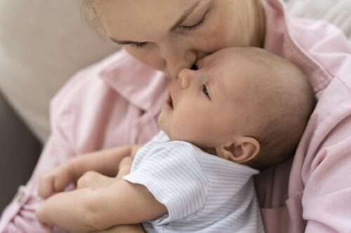 An adult holds a baby close and gently presses their face to the baby’s head.