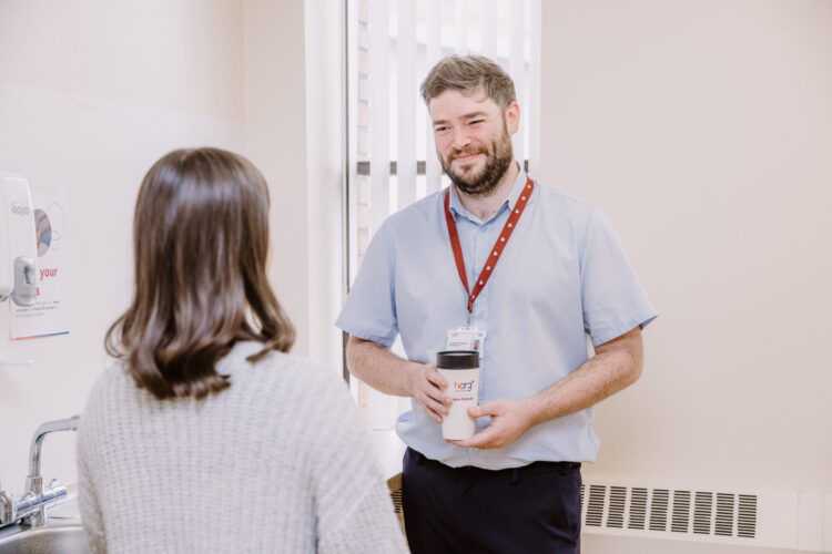 A healthcare worker is smiling, holding a coffee mug.
