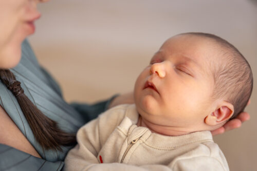 A newborn baby sleeps while being held in an adult’s arms.