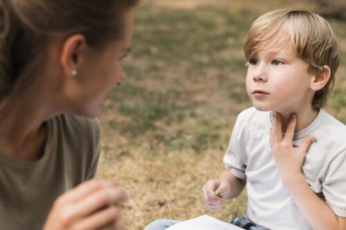 Adult talking to a child while the child touches their throat.