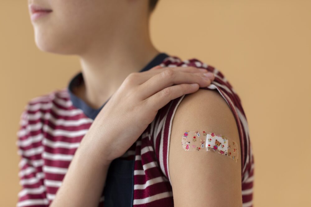 A child’s upper arm with a decorative adhesive bandage covering an injection site.