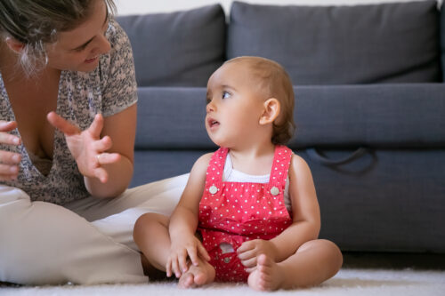 Adult interacting with a baby sitting on the floor