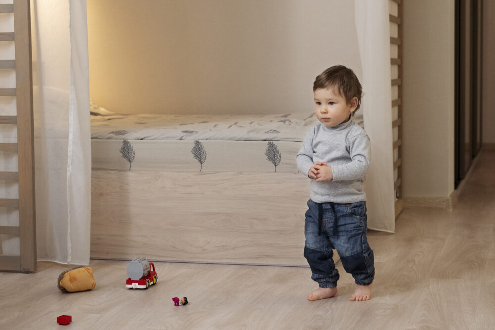 Toddler standing barefoot in a bedroom near toys.
