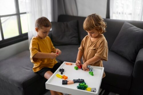 Two young children sit at a small table playing with building blocks.