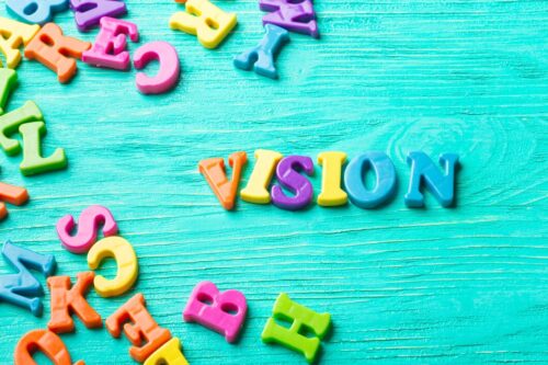 Colourful plastic letters scattered on a turquoise surface, spelling the word ‘VISION’.