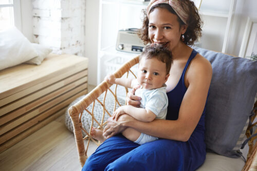 Parent holding a baby in a wicker chair at home.
