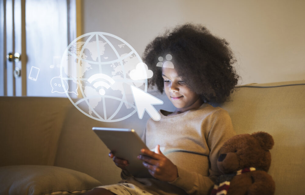 A child sits on a sofa using a tablet, with a teddy bear beside them and digital icons overlaid on the screen.